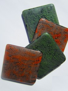 Set of four coasters with green and orange bubble effect on black glass.